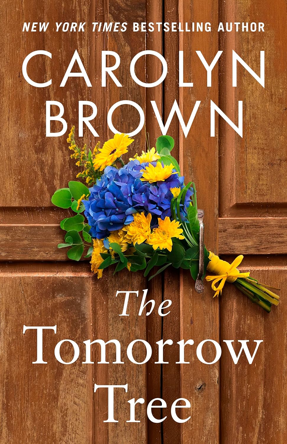 The evocative, atmospheric book cover of The Tomorrow Tree by Carolyn Brown, showing a sprawling, sun-dappled ancient oak tree that anchors the story's themes of family roots and legacy.